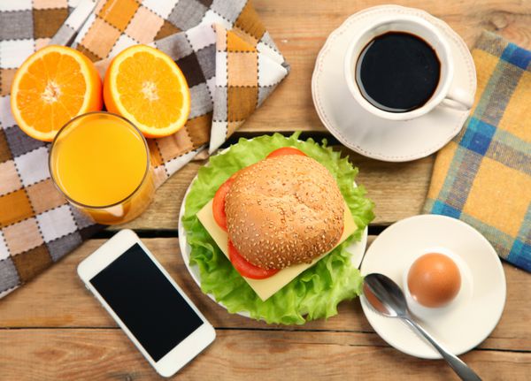 صبحانه و گوشی موبایل روی میز چوبی