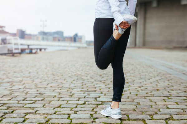 نمای پایین از یک زن جوان خوش اندام که پای خود را قبل از دویدن در خیابان های شهر دراز می کند آمادگی برای تمرین دویدن