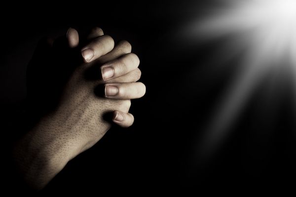 دست های دعا در تاریکی با نور بر دست ها است