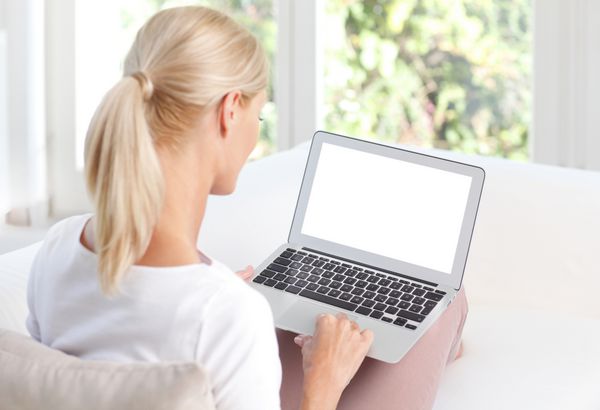 پرتره زن میانسالی که از لپ تاپ صفحه خالی خود استفاده می کند در حالی که پشت به پشت روی مبل خانه نشسته است