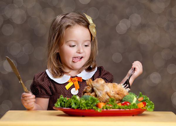 شام مراسم شکرگزاری دختر کوچولوی شایان ستایشی که پشت یک میز کوچک با یک بوقلمون کوچک مرغ روی تختی از سبزیجات و سبزیجات دیگر نشسته است فضایی برای متن شما