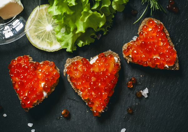ساندویچ هایی به شکل قلب با خاویار سالمون قرمز و کره روی نان چاودار نمای بالا