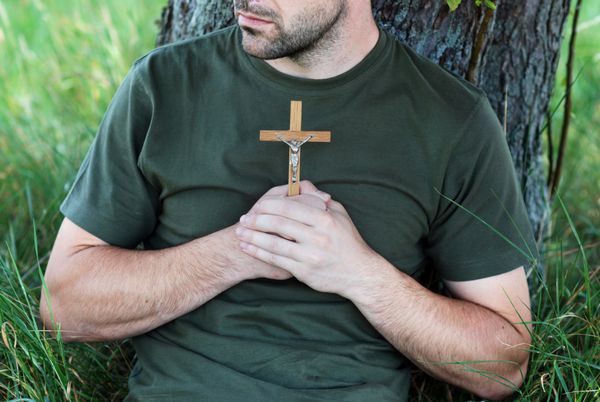 مرد صلیب دار زیر درخت دعا می کند