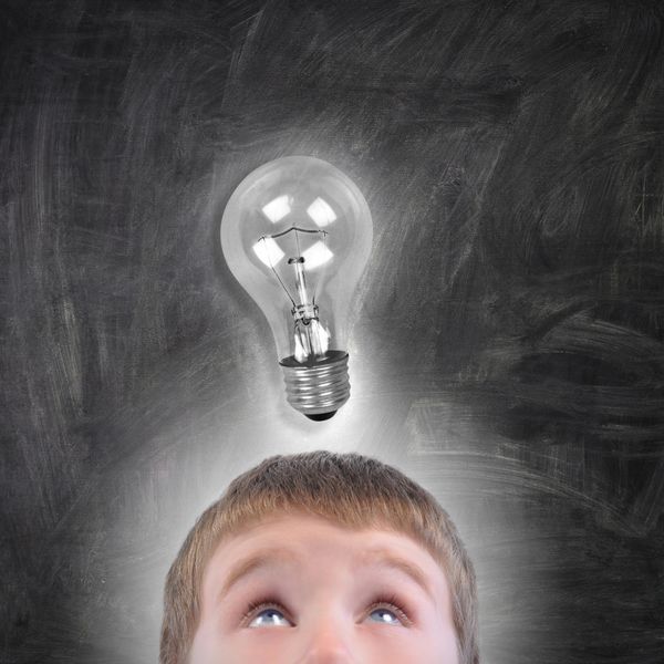 یک پسر مدرسه ای جوان به یک لامپ درخشان بالای سرش روی تخته سیاه سیاه نگاه می کند از آن برای یک ایده یا مفهوم آموزشی استفاده کنید