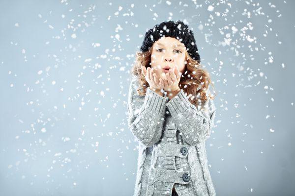 پرتره زمستانی دختر کوچولوی بامزه ای که لباس های گرم دنج استودیو با برف پوشیده است