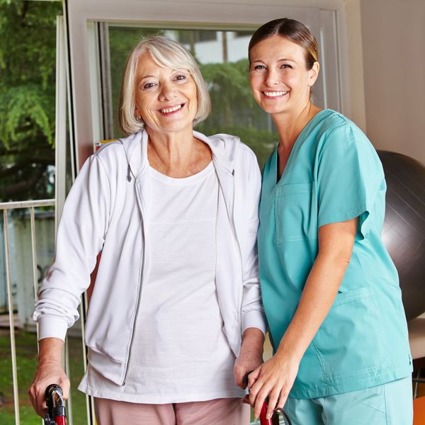 زن مسن شاد با واکر و پرستار در فیزیوتراپی