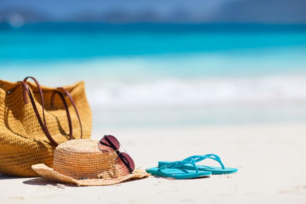 کلاه حصیری کیف عینک آفتابی و دمپایی در یک ساحل استوایی
