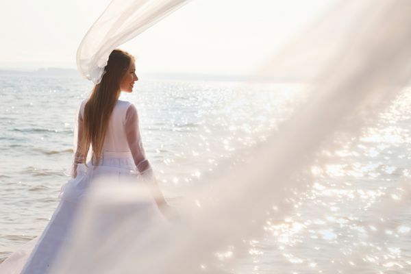 عروس جوان در نزدیکی آب گازدار با حجاب بلند پرواز ایستاده است تمرکز انتخابی
