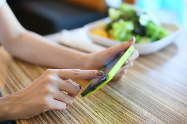 زن با استفاده از تلفن همراه روی میز غذا