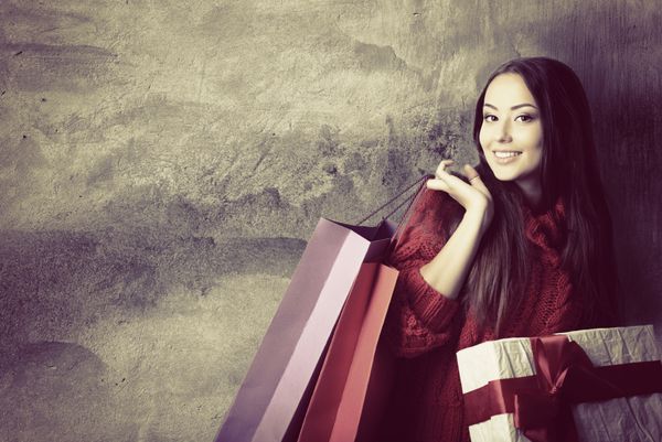 زن جوان زیبا که کیسه‌های خرید رنگی و جعبه هدیه را روی دیوار بتونی گرانج مفهوم فصلی تعطیلات رنگ‌آمیزی گرفته است