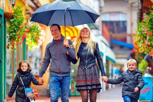 خانواده شاد در حال قدم زدن زیر باران در خیابان رنگارنگ