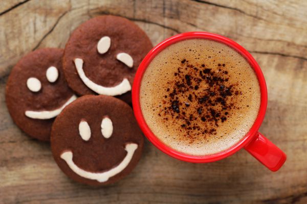 صبح بخیر یا مفهوم پیام روز خوبی داشته باشید - فنجان قهوه کف‌دار قرمز روشن با کوکی‌های شکلاتی خندان