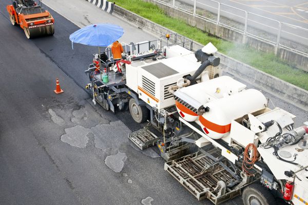 کارگران آسفالت با بیل در راه سازی و غلتک های جاده در حین کار آسفالت کاری برای تعمیر خیابان حمل و نقل سیاهپوش