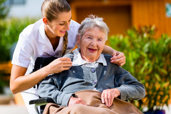 زن مسن در خانه سالمندان با پرستار در باغ روی ویلچر نشسته است