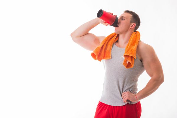 مرد بدنساز که روی پس‌زمینه سفید ژست گرفته است مرد شیکری برای نوشیدنی در دست گرفته است مردی در حال نوشیدن یک شیک پروتئین آب اسیدهای آمینه از شیکر ورزش تغذیه ورزشی افزودنی های غذایی