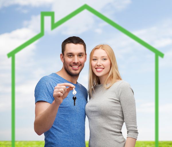مفهوم عشق خانه مردم و خانواده - زوج خندان که کلید خانه را بر فراز خانه سبز و آسمان آبی با پس زمینه چمن در دست دارند