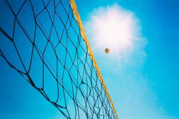 توپ والیبال روی تور در پس زمینه آسمان آفتابی آبی تابستان توپ در حال پرواز در هوا در ساحل