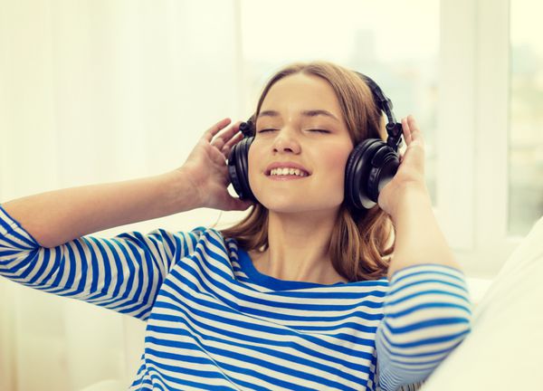 مفهوم فناوری موسیقی و شادی - دختر جوان خندان در هدفون در خانه