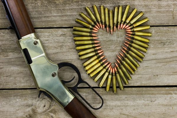 گلوله هایی به شکل قلب در کنار تفنگ در زمینه چوبی روستایی