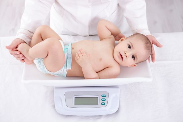 متخصص اطفال زن در حال وزن کردن نوزاد شایان ستایش در مطب