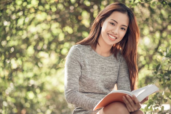 پرتره زن شاد و جذاب ویتنامی در حال خواندن کتاب در فضای باز