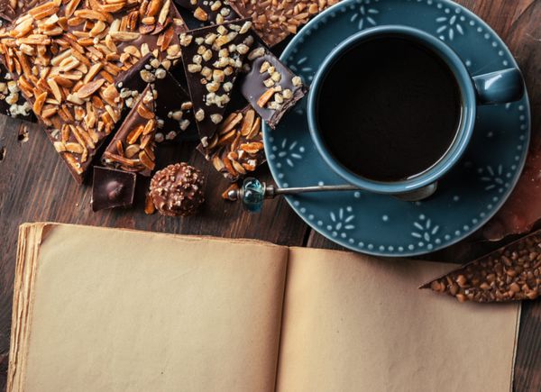 فنجان قهوه مجموعه ای از شکلات های خوب تیره شکلات شیری و کتابی برای یادداشت روی میز چوبی