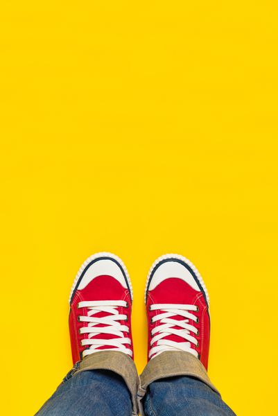 مفهوم پا از بالا فرد نوجوان با کفش‌های کتانی قرمز که روی پس‌زمینه زرد ایستاده b lank copy sp در جلو