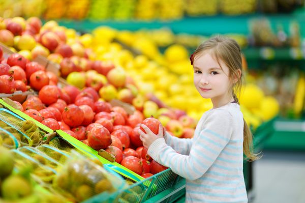 دختر کوچکی که در یک فروشگاه مواد غذایی یا یک سوپرمارکت انار انتخاب می کند