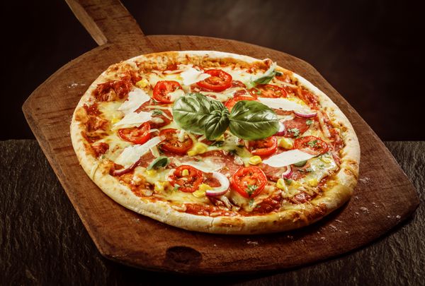 نمای بالا از پیتزا مارگریتای تازه پخته شده با گوجه فرنگی پنیر و ریحان تازه روی پارو چوبی