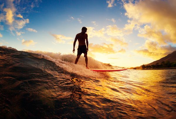 موج سواری در غروب مرد جوان سوار بر موج در غروب آفتاب سبک زندگی فعال در فضای باز