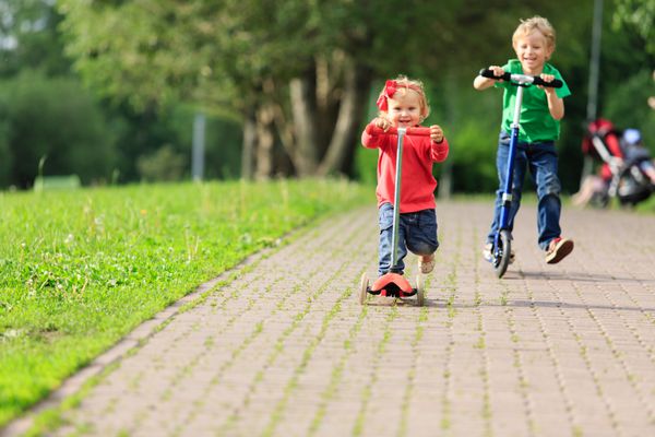 پسر کوچک و دختر نوپا اسکوتر سواری در پارک تابستانی ورزش کودکان