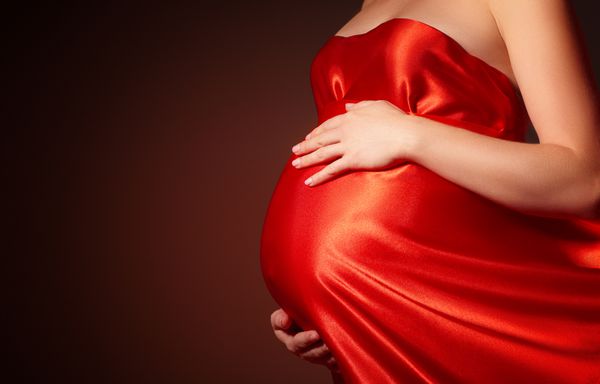 شکم زیبای زن باردار با لباس ابریشمی قرمز در حال وزیدن