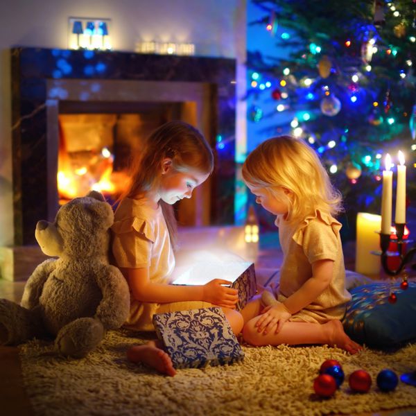 دختران کوچک شایان ستایشی که در زمستان یک هدیه کریسمس جادویی توسط یک درخت کریسمس در اتاق نشیمن دنج باز می کنند