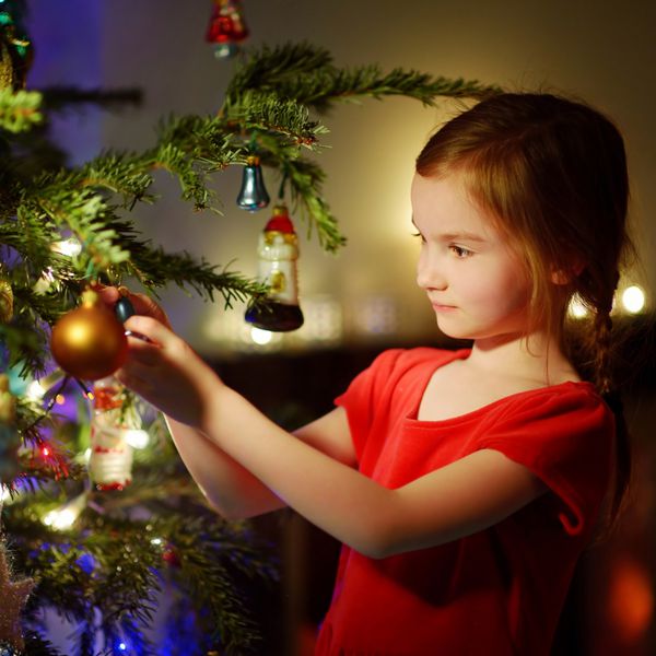 دختر کوچولوی شایان ستایشی که درخت کریسمس را با گلدان های شیشه ای رنگارنگ در خانه تزئین می کند