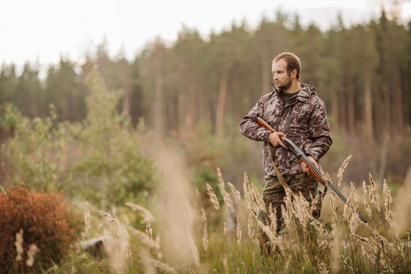 شکارچی مرد با لباس استتار آماده شکار با تفنگ شکاری