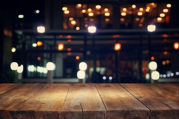 تصویری از میز چوبی در مقابل پس زمینه تار انتزاعی چراغ های رستوران