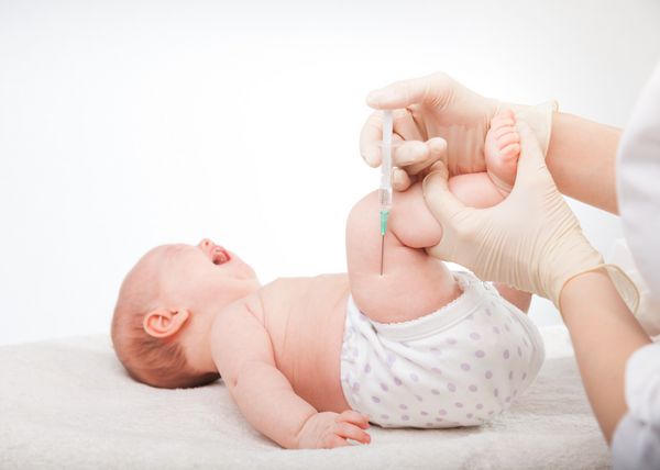 نمای نزدیک از پزشک اطفال که به یک نوزاد دختر سه ماهه تزریق عضلانی در پا انجام می دهد
