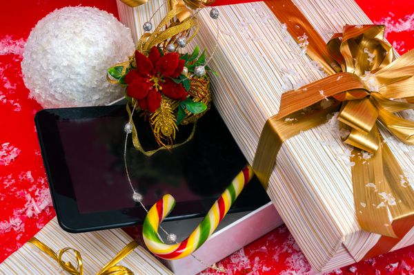 تبلت و آب نبات بهترین هدیه کریسمس در جعبه روی پس زمینه قرمز