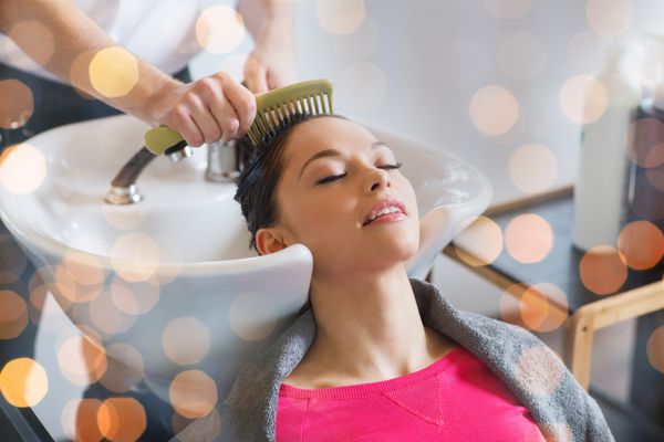 زیبایی مراقبت از مو و مفهوم افراد - زن جوان شاد با آرایشگر که موهای خیس را بعد از شستن در سالن در نور تعطیلات شانه می کند