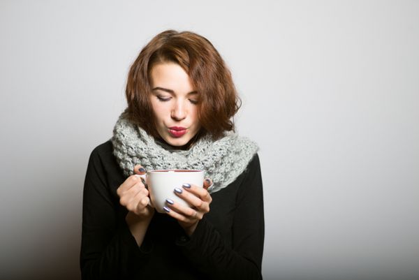 دختر زیبا در حال نوشیدن قهوه یا چای برای گرم نگه داشتن در زمستان مفهوم مدیر دفتر در پس زمینه خاکستری جدا شده است