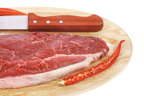 فیله گوشت گاو خام تازه با فلفل قرمز قرمز و چاقو روی بشقاب چوبی جدا شده روی پس زمینه سفید