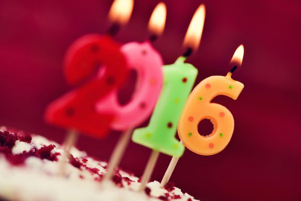 نمای نزدیک چهار شمع اعدادی روشن با رنگ های مختلف که شماره 2016 را به عنوان سال جدید روی یک کیک تشکیل می دهند