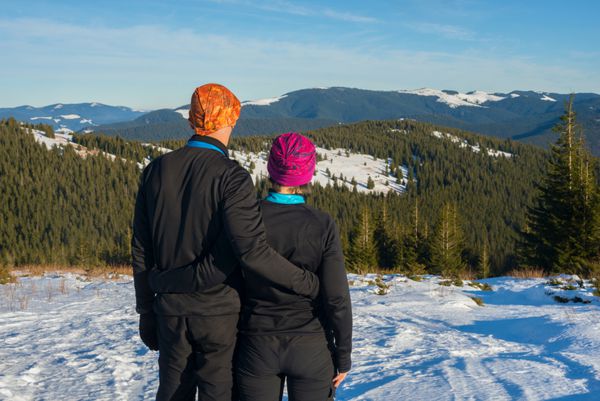 زوج کوهنورد در کوه های زمستانی ایستاده اند و به دره نگاه می کنند