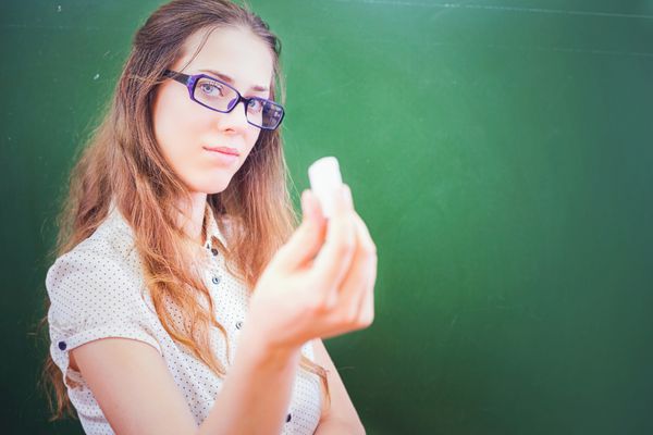 زن جوان زیبا - معلم یا دانش آموز که یک گچ را نزدیک تخته سیاه سبز در کلاس درس در مدرسه دانشگاه نگه داشته است بریم سراغ تخته سیاه