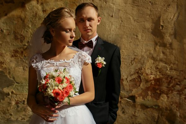 ازدواج تازه ازدواج کرده در فضای باز ژست عروس و داماد روز آفتابی زن و مردی که نزدیک دیوار ایستاده اند زنی با چشمان بسته