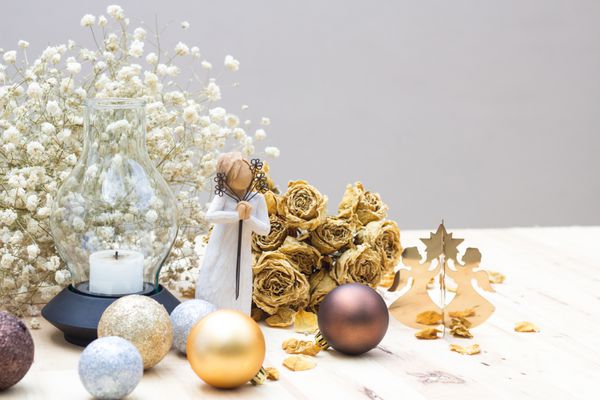 تزیین کریسمس فرشته طلایی و زنی چوبی با لباس سفید که گل در دست دارد و روی گل و رز سفید چوبی و خشک شده دعا می کند