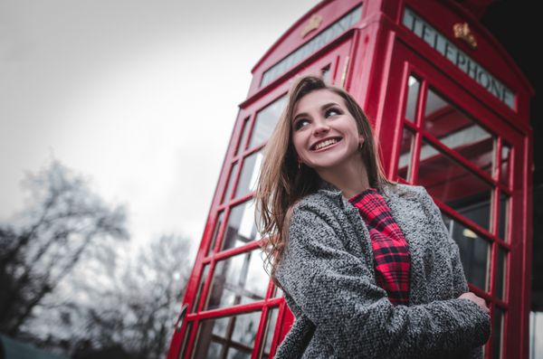 زن جوان با غرفه تلفن قرمز پرتره زن لبخند زیبا و خوشحال لبخند زن جوان معمولی ایستاده در لندن انگلستان بریتانیا