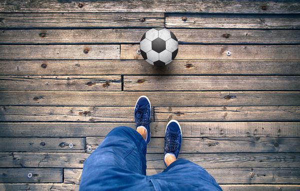 نقطه نظر پاهای مردی با توپ فوتبال روی کف کاشی چوبی قدیمی