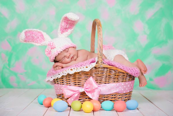 دختر بچه تازه متولد شده در لباس خرگوش رویاهای شیرینی روی سبد حصیری می بیند تعطیلات عید پاک