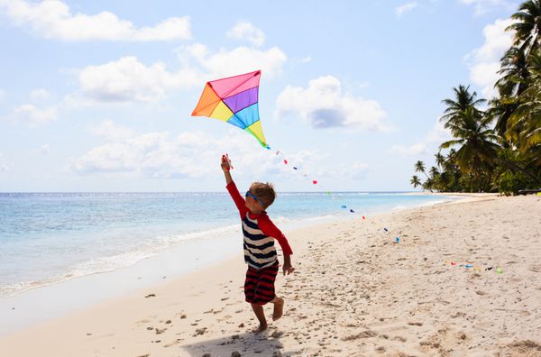 پسر کوچک در حال پرواز بادبادک در ساحل استوایی
